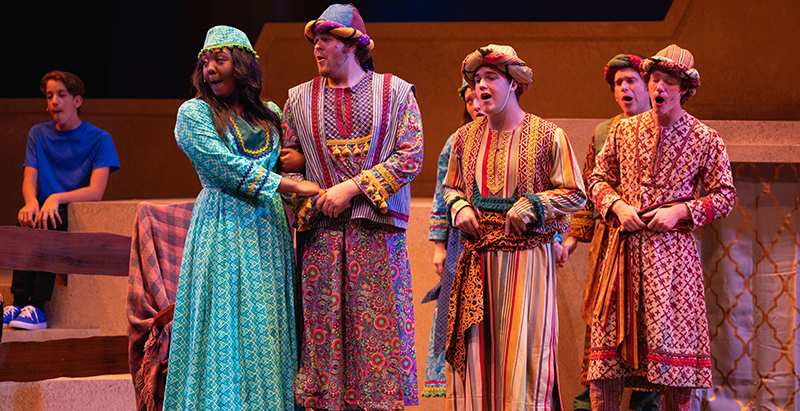 chorus members from joseph and the amazing technicolor dreamcoat wearing biblical dress, singling on stage holding hands