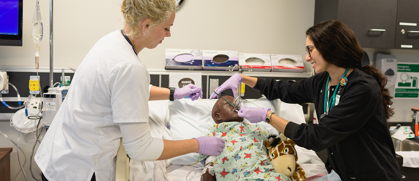two practical nurse students practicing on a dummy patient lying on a gurney