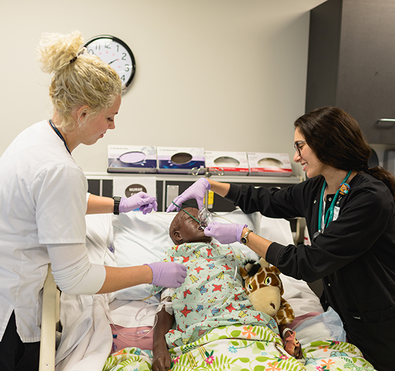 two practical nurse students practicing on a dummy patient lying on a gurney