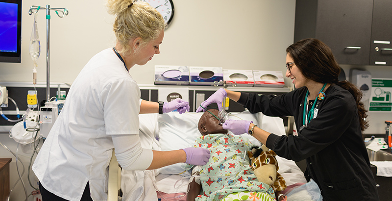 two practical nurse students practicing on a dummy patient lying on a gurney