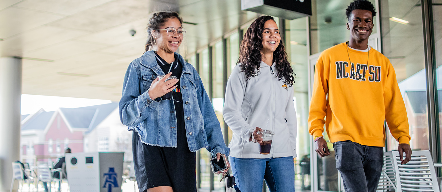 three NC A&T students smiling and walking on covered walkway near campus bistro