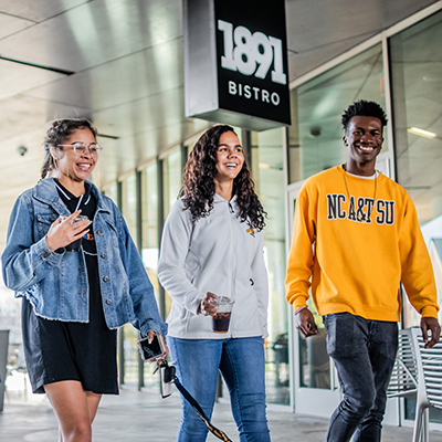 three NC A&T students smiling and walking on covered walkway near campus bistro