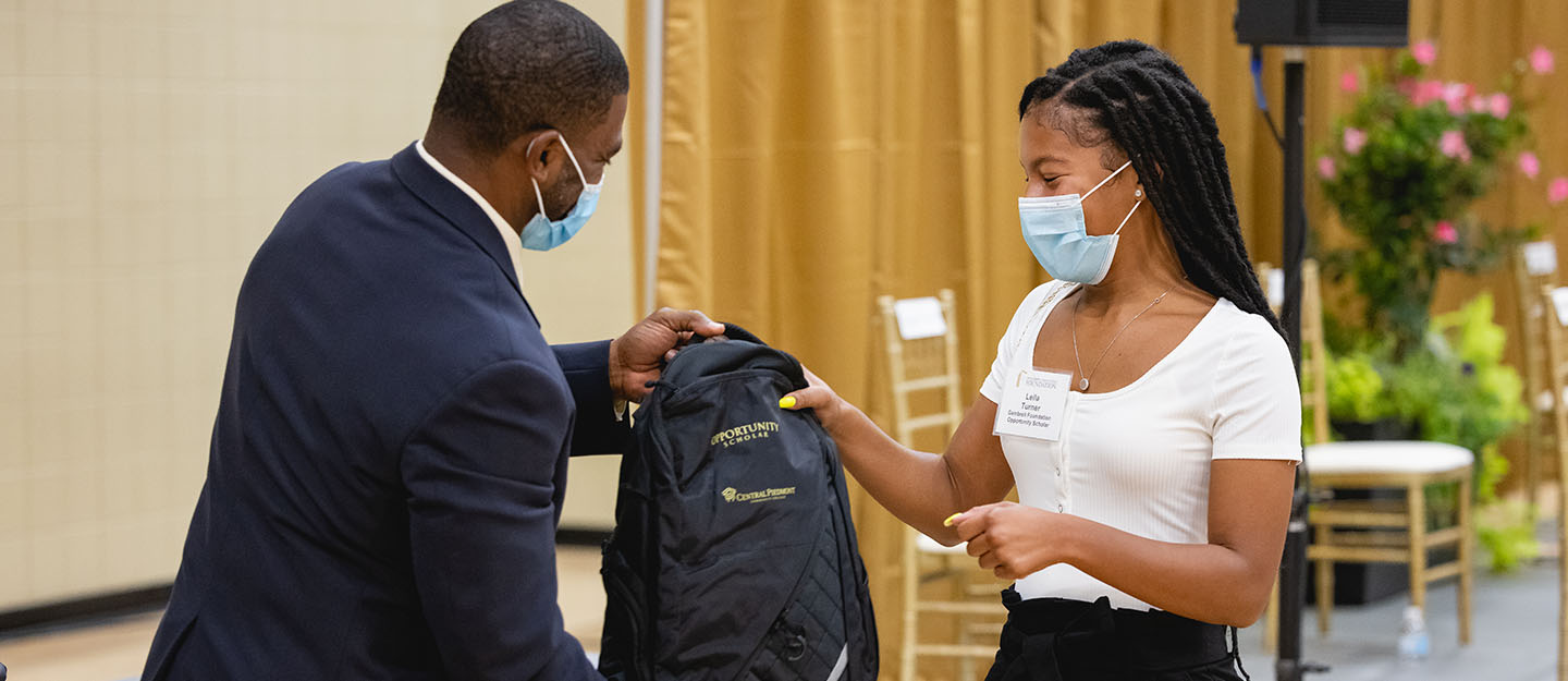 mentoring student in professional dress being handed backback as gift at mentoring event