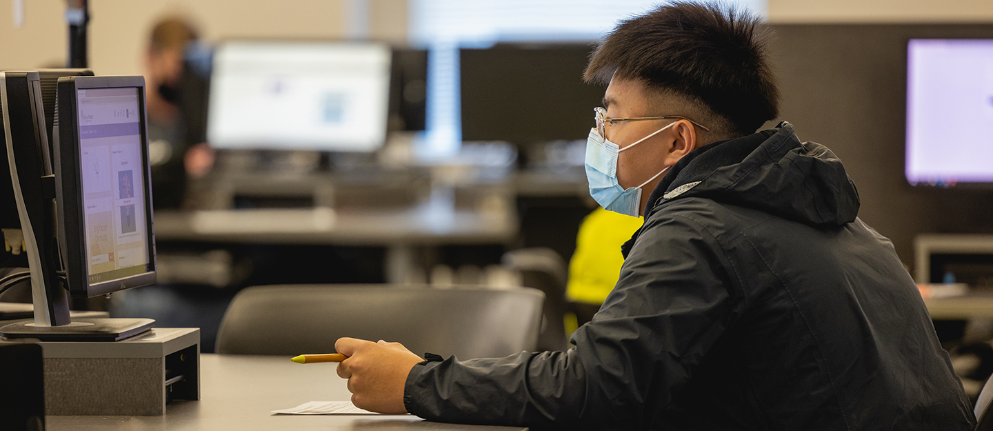 a student wearing glasses and a mask working at a computer