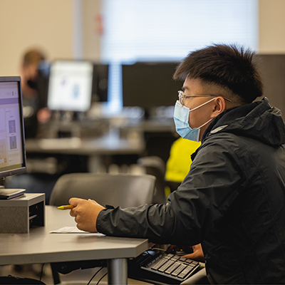 a student wearing glasses and a mask working at a computer