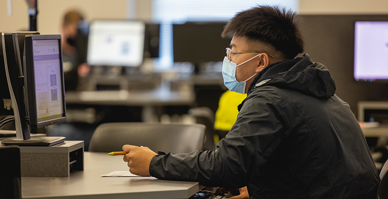 a student wearing glasses and a mask working at a computer