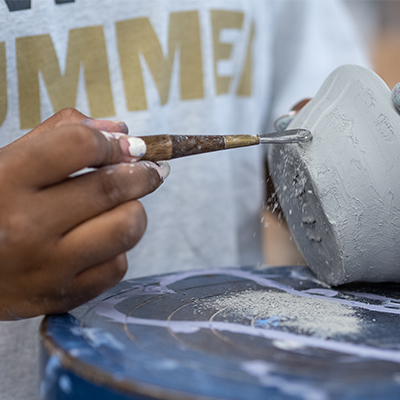 hand of a diverse summer camp student working with pottery