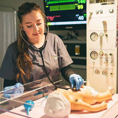 Central Piedmont healthcare program student wearing scrubs and gloves using stethoscope on baby dummy