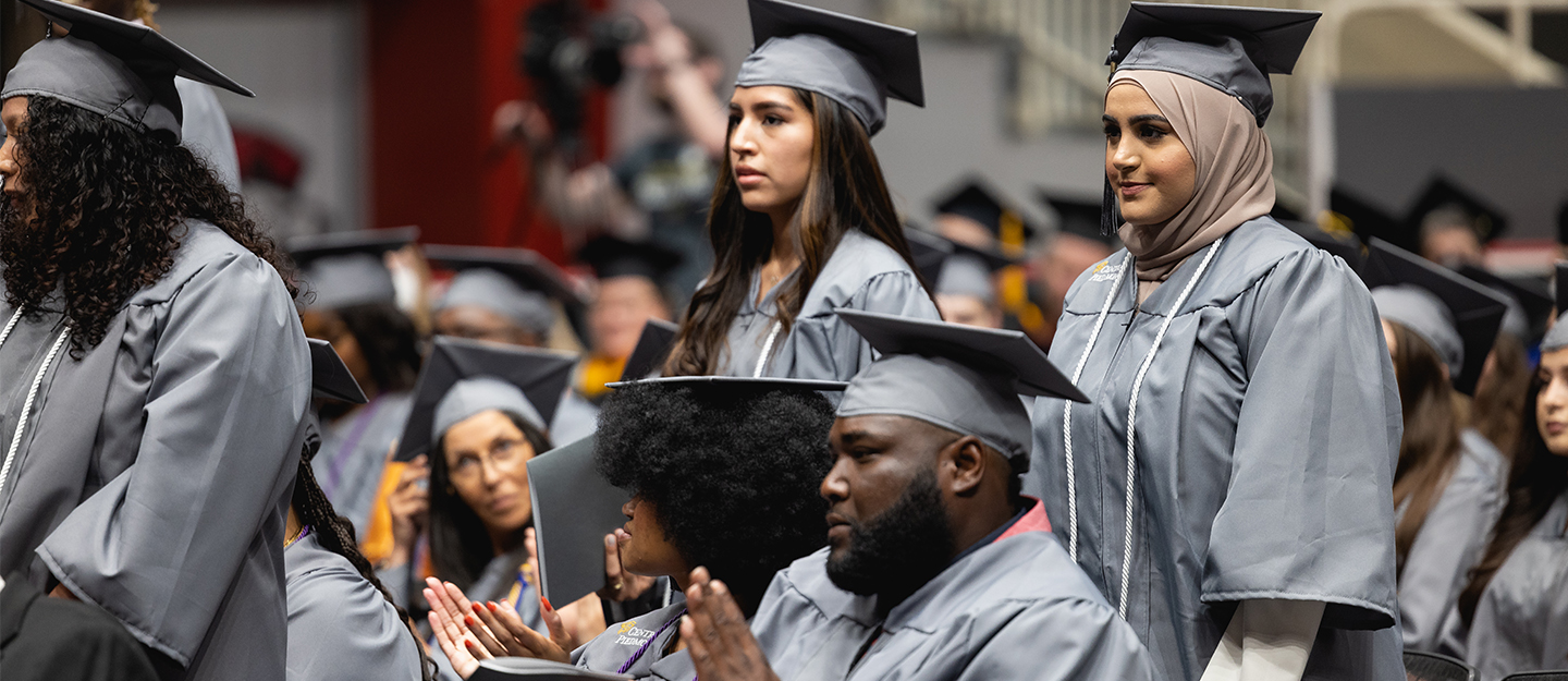 diverse students in cap and gown standing at graduation