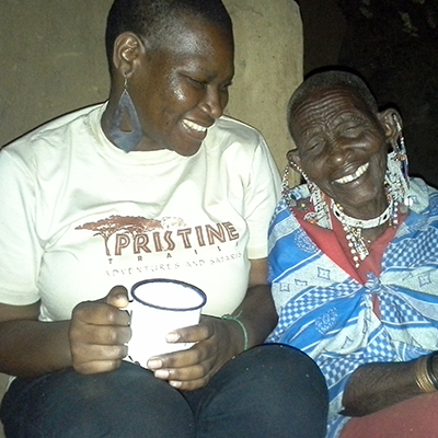 two African people sitting in the dark, one with a cup in hand, both smiling