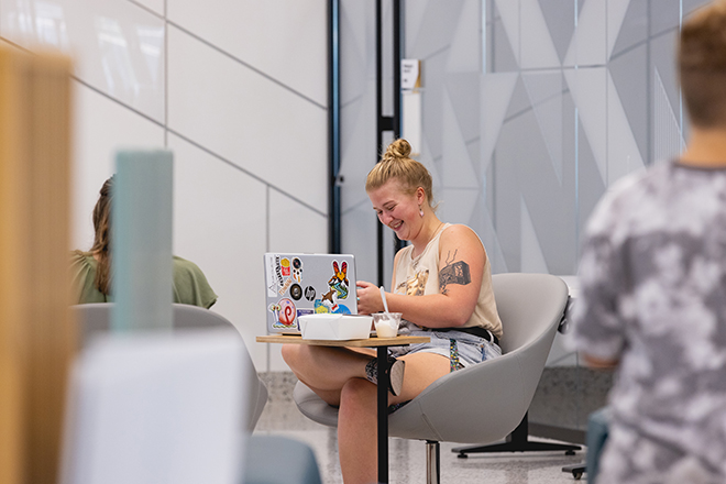 Female student in the Parr Center smiling with her laptop