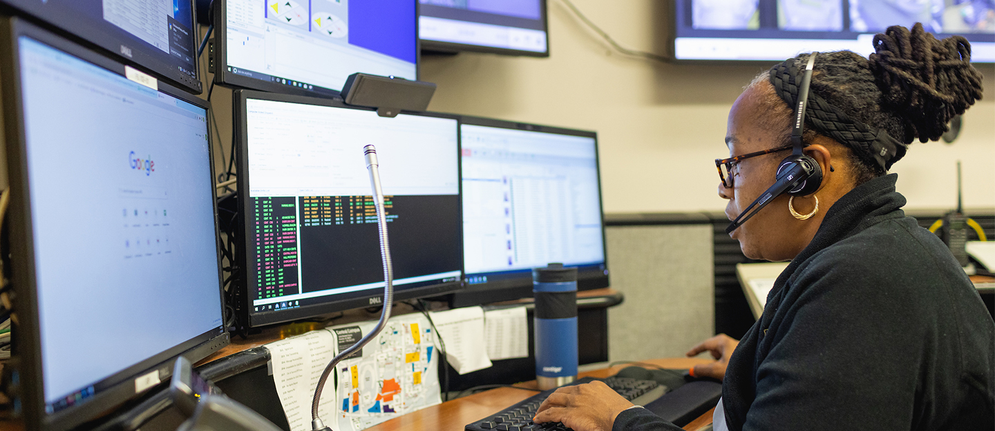 Central Piedmont college diverse security staff member at desk with headset looking at security monitors