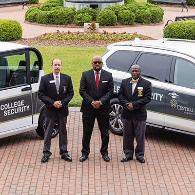 Central Piedmont college security leadership in suits in front of security vehicles