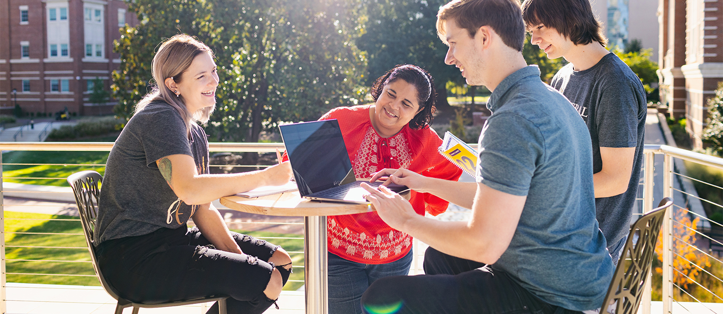 Four students sitting outdoors working on a laptop