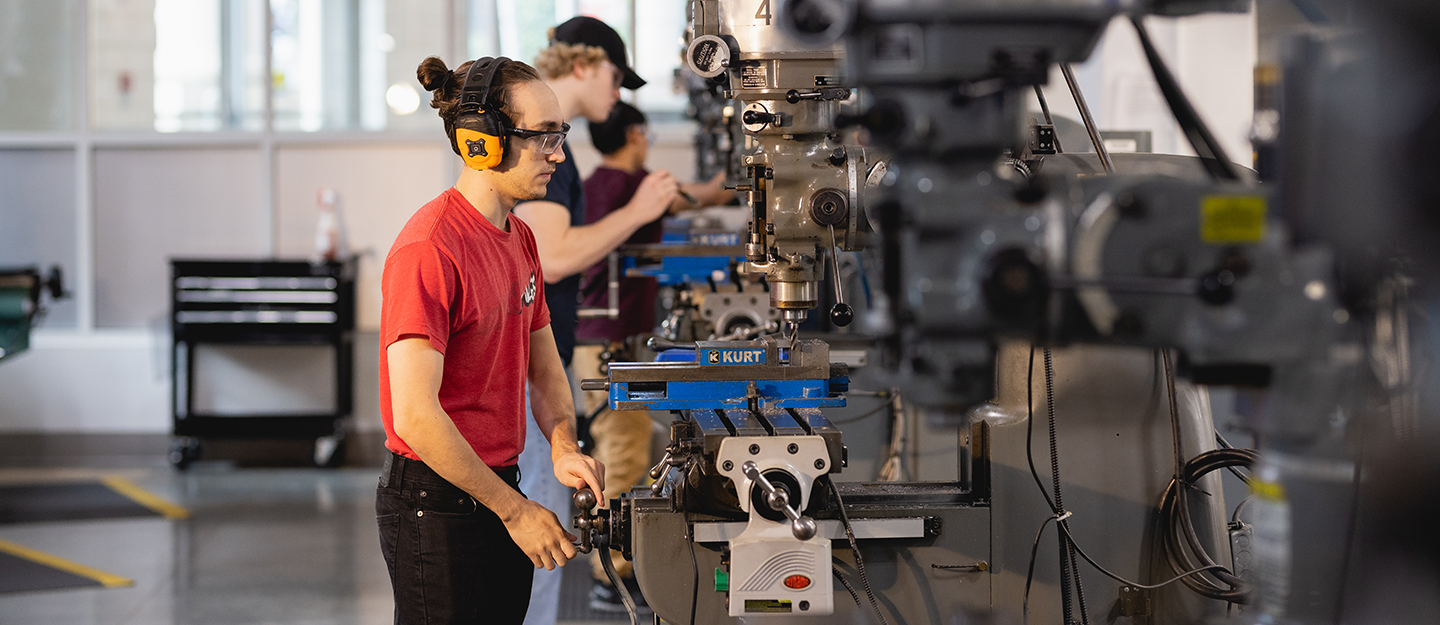 computer-integrated machining technology student standing in front of machining equipment with headphones and safety glasses on