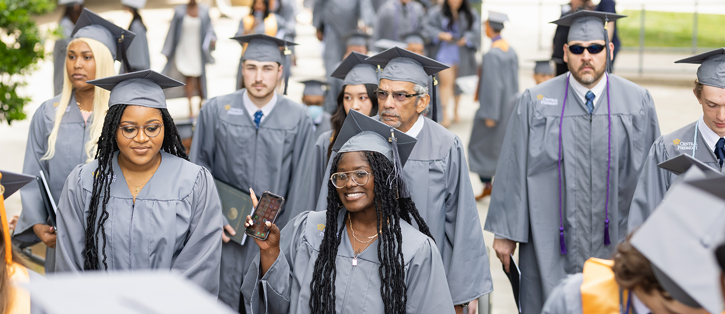 group of diverse Central Piedmont graduates in cap and gown walking outside at graduation ceremony