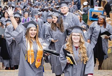 Graduate in a cap and gown holding up her hand in celebration along with many other graduates