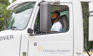 Student driver looking in the side mirror, sitting behind the wheel of a 18-wheeler truck with the Central Piedmont logo on the door.