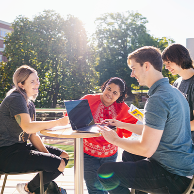 Students sitting outside on a sunny day working on a laptop 
