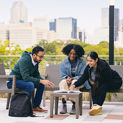 Three students sitting outside the Parr Center and reading a book 