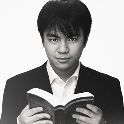 Black and white photo of student holding a book and looking into the camera