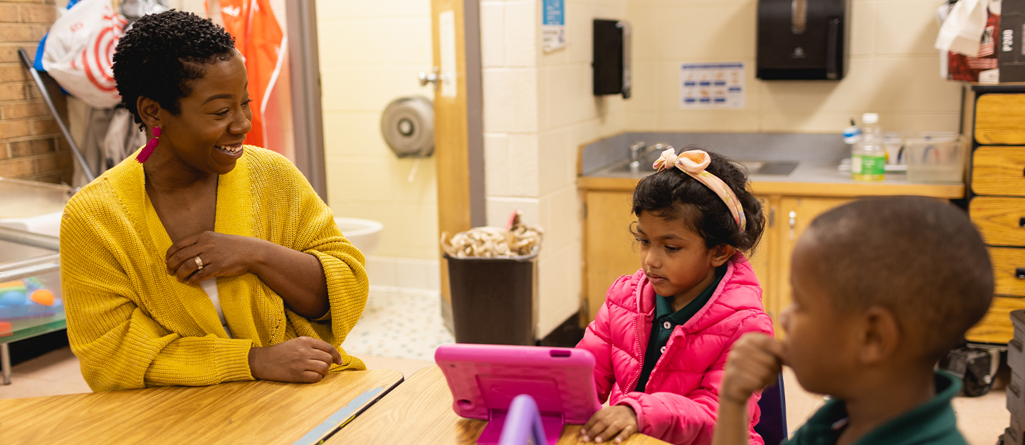 WTVI representative helping children learn at a desk using a tablet 