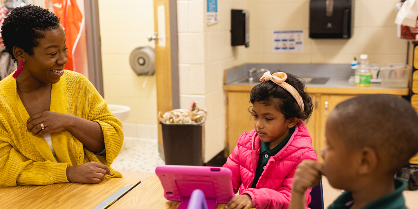 WTVI representative helping children learn at a desk using a tablet 