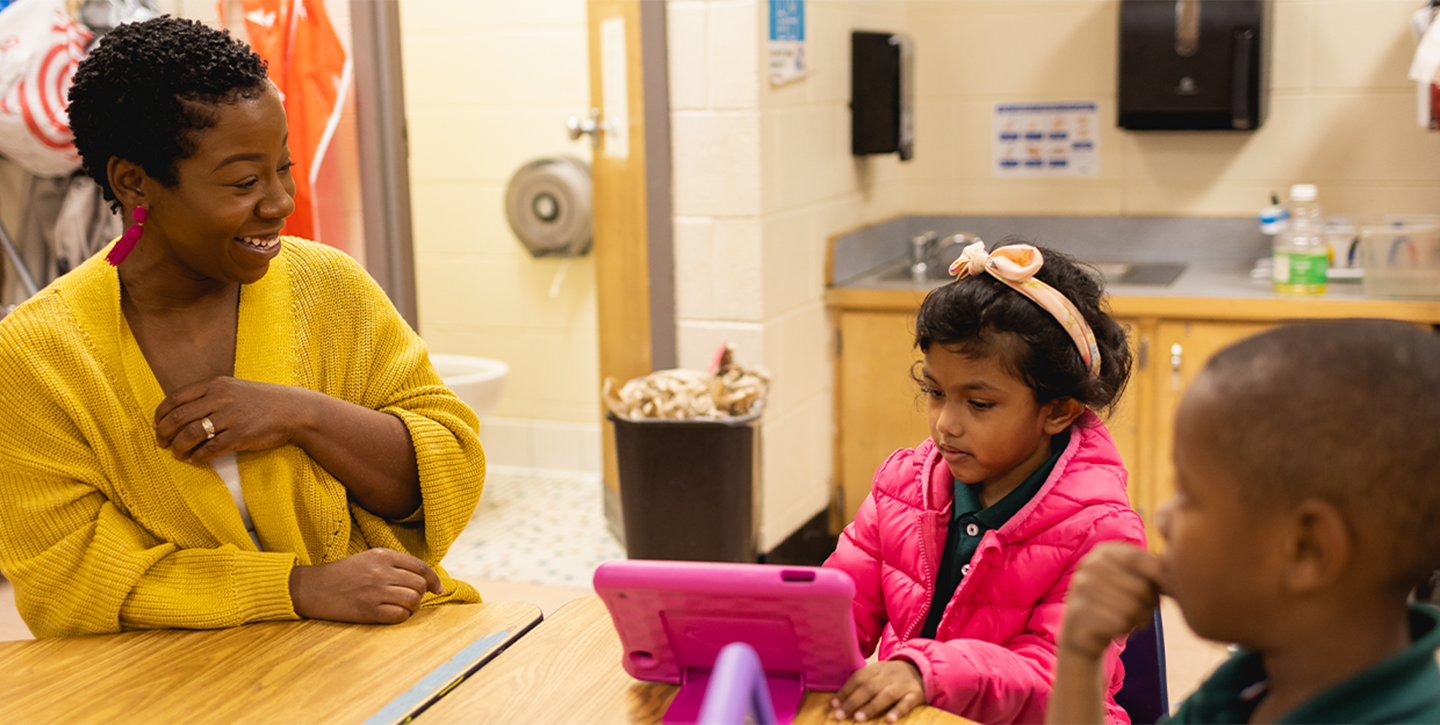 WTVI representative helping children learn at a desk using a tablet 