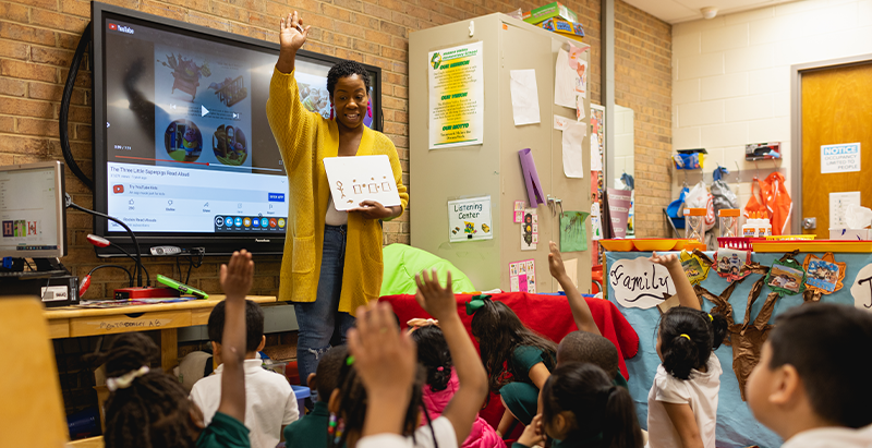 Teacher asking question to little children who have their hand raised