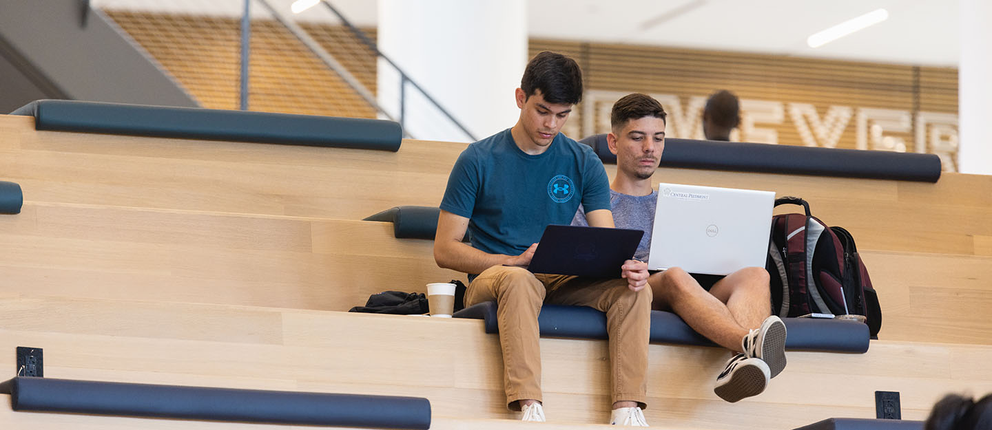 two diverse students sitting in front of laptops on steps in Parr Center at Central Piedmont Community College.