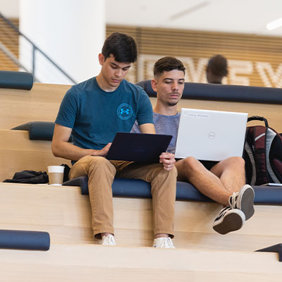 two diverse students sitting in front of laptops on steps in Parr Center at Central Piedmont Community College.