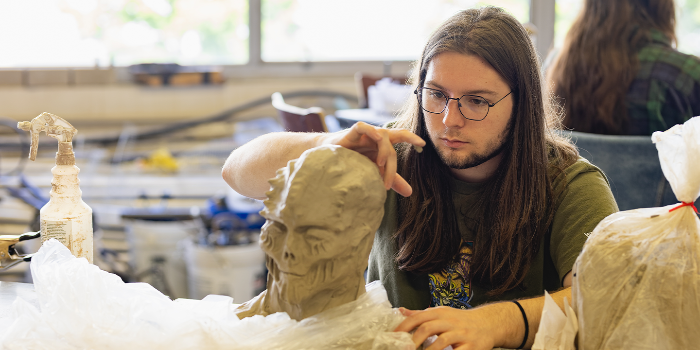 Person with glasses molding an alien head out of clay 