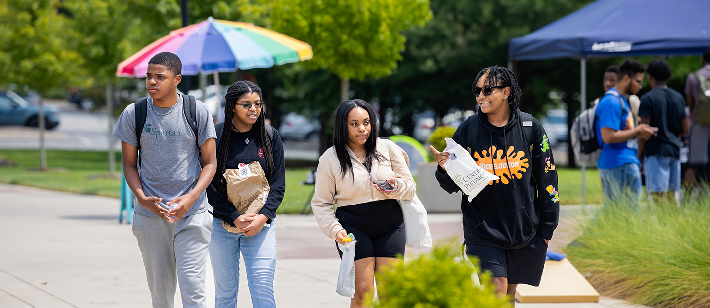 Four middle college students walking campus 