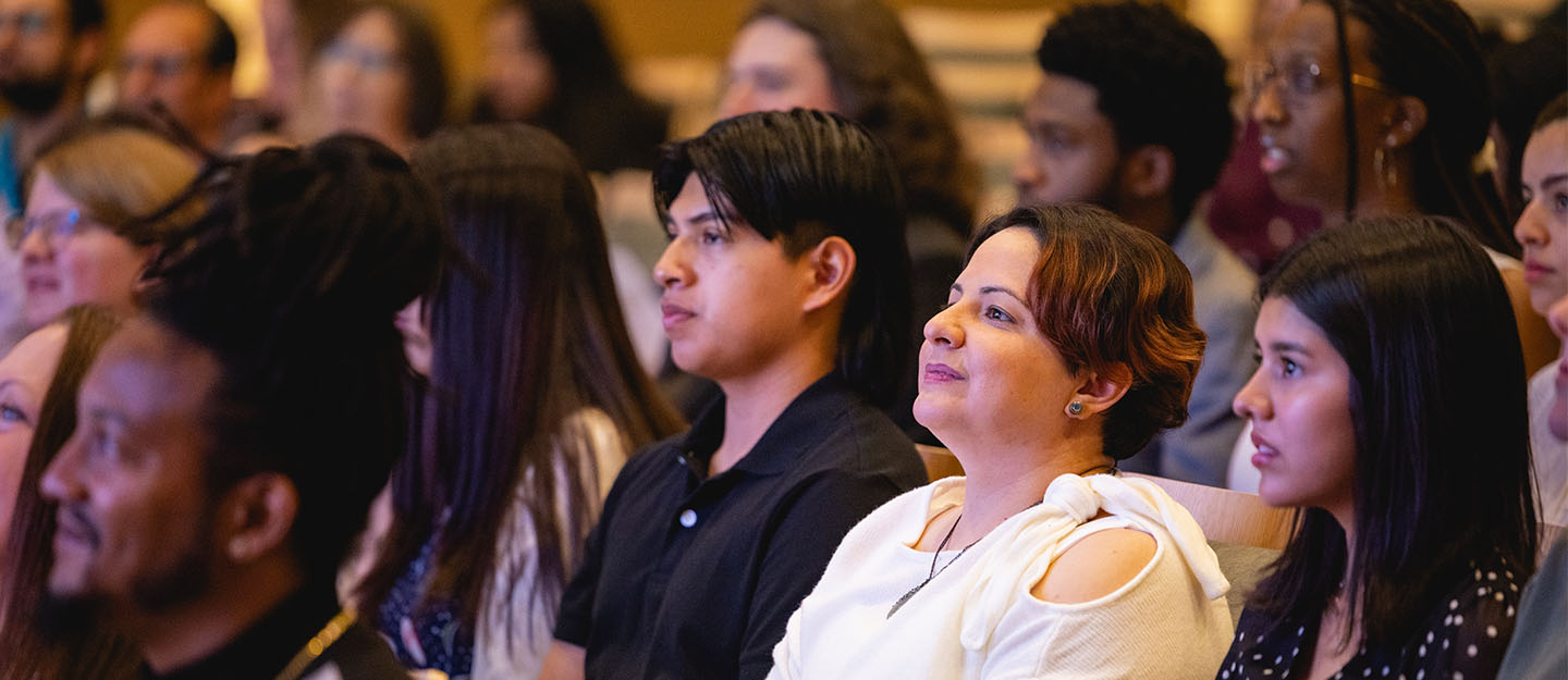 diverse students sitting in auditorium seating facing the front and listening to presentation
