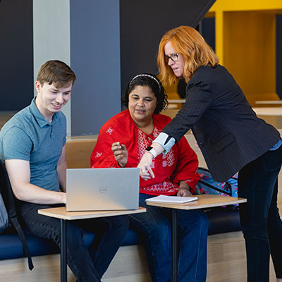 Library staff helping two students looking at a laptop