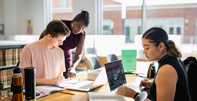 An instructor assisting two students at a table 