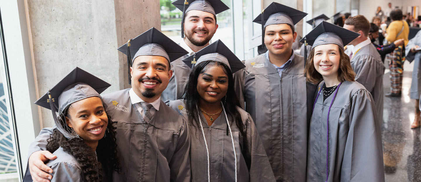 diverse graduates in gray cap and gown standing smiling in the camera at spring graduation at Central Piedmont Community College