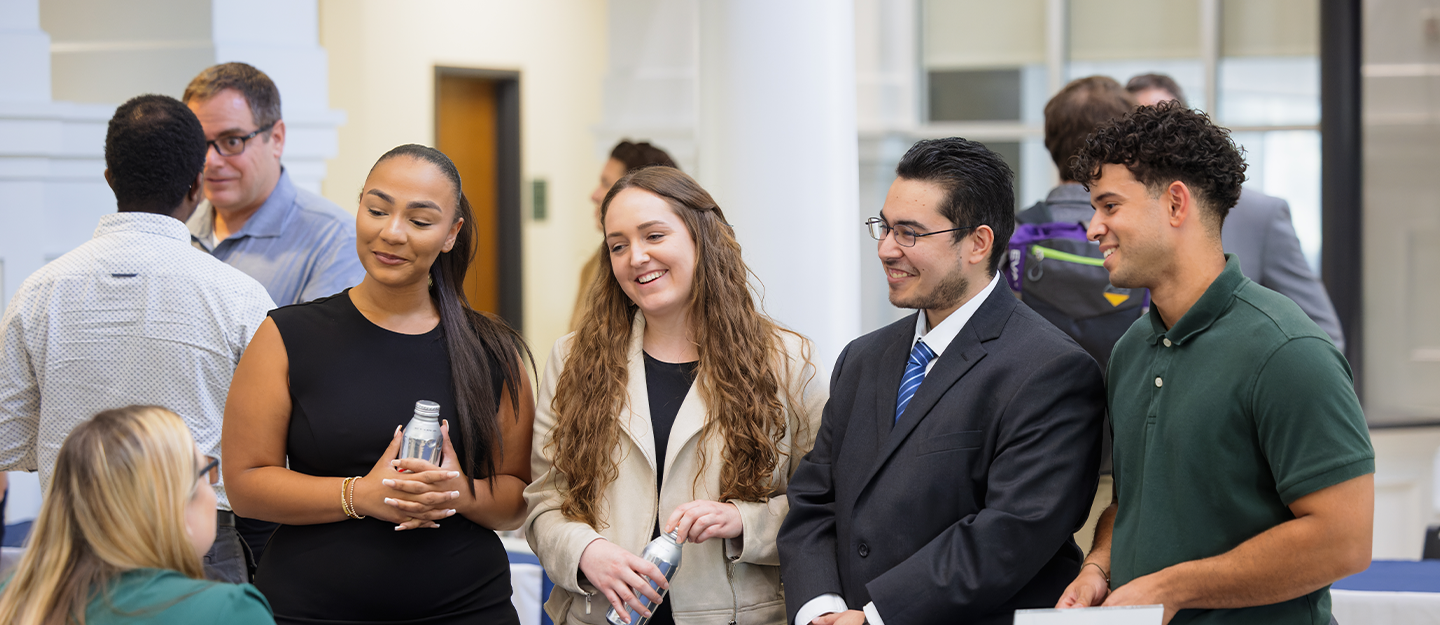 5 people smiling and standing around speaking with each other 