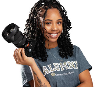 Student standing in a Central Piedmont shirt holding a camera 