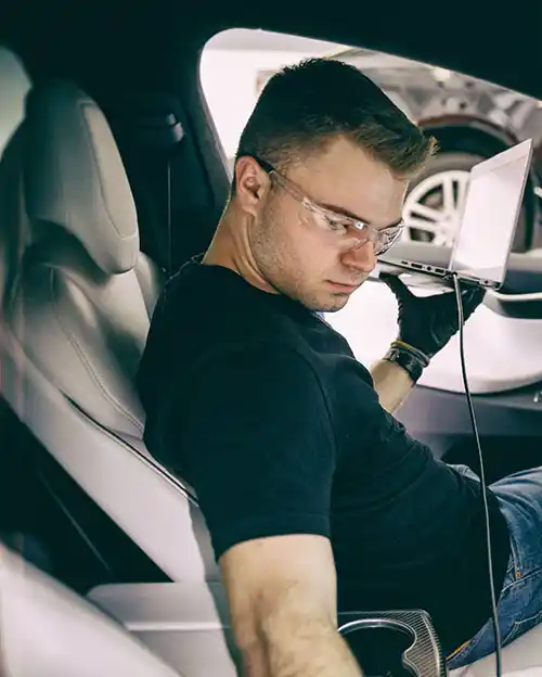 automotive systems technology student inside car with laptop in hand 