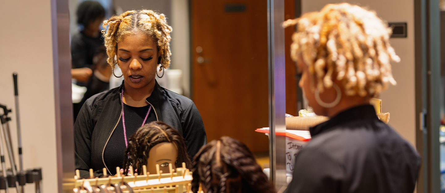 cosmetology student practicing on a mannequin in the mirror
