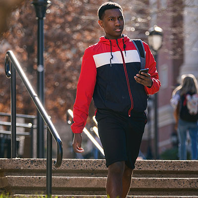 diverse student walking to class with backpack and phone in his hand 