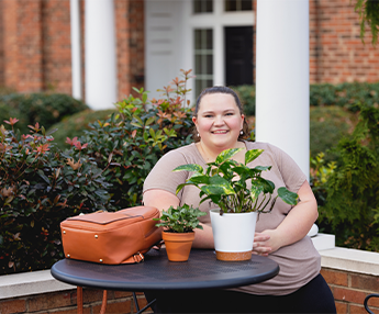 Student seated at table with a green plant