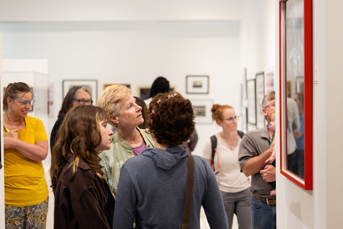 Visitors viewing framed artwork on the walls of a campus gallery