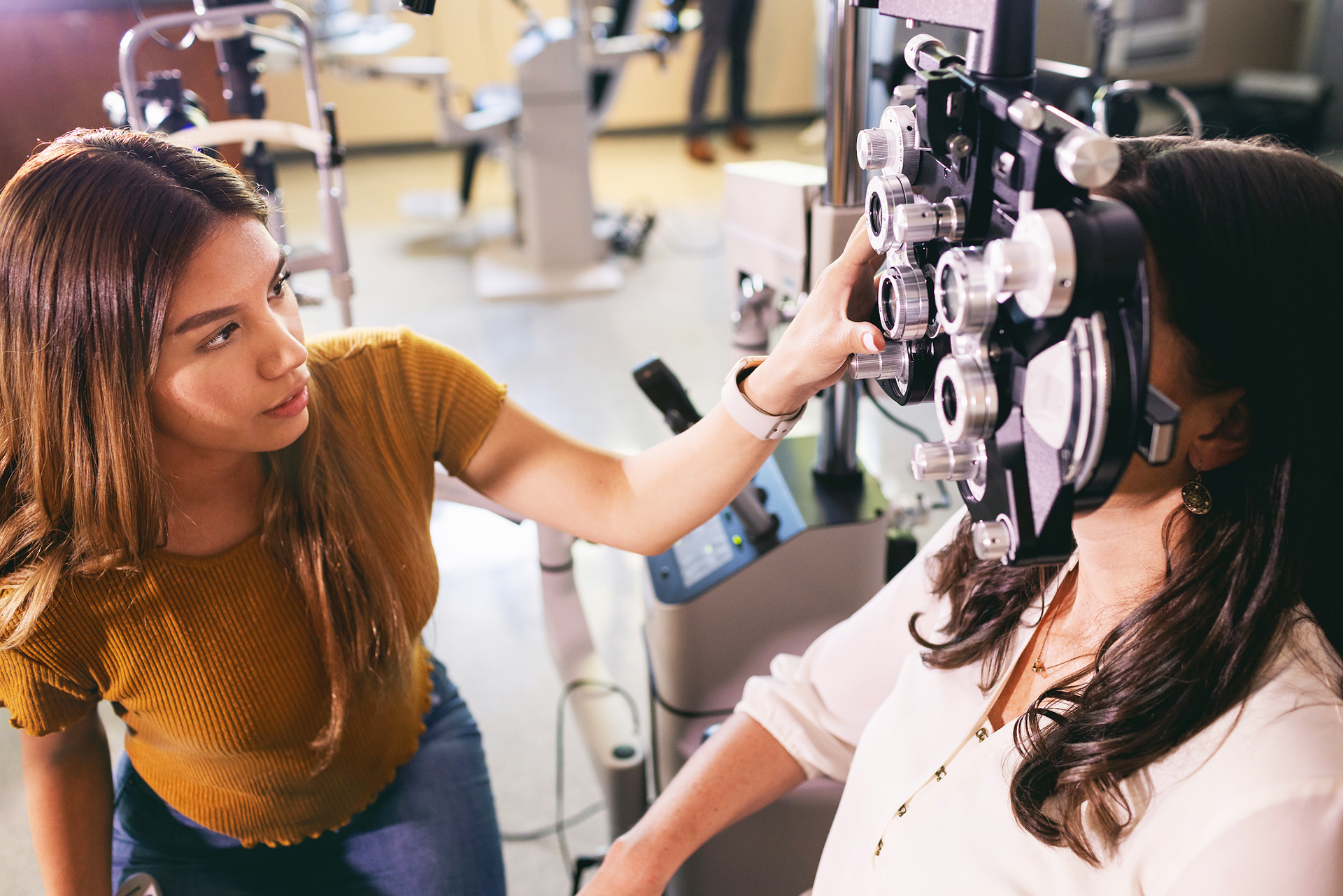 Central Piedmont student working with other student looking through optometry phoropter machine.