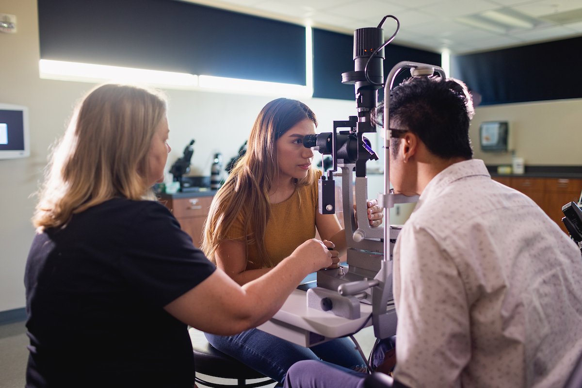 Ophthalmic students examining a patient using eye-testing equipment in the clinic