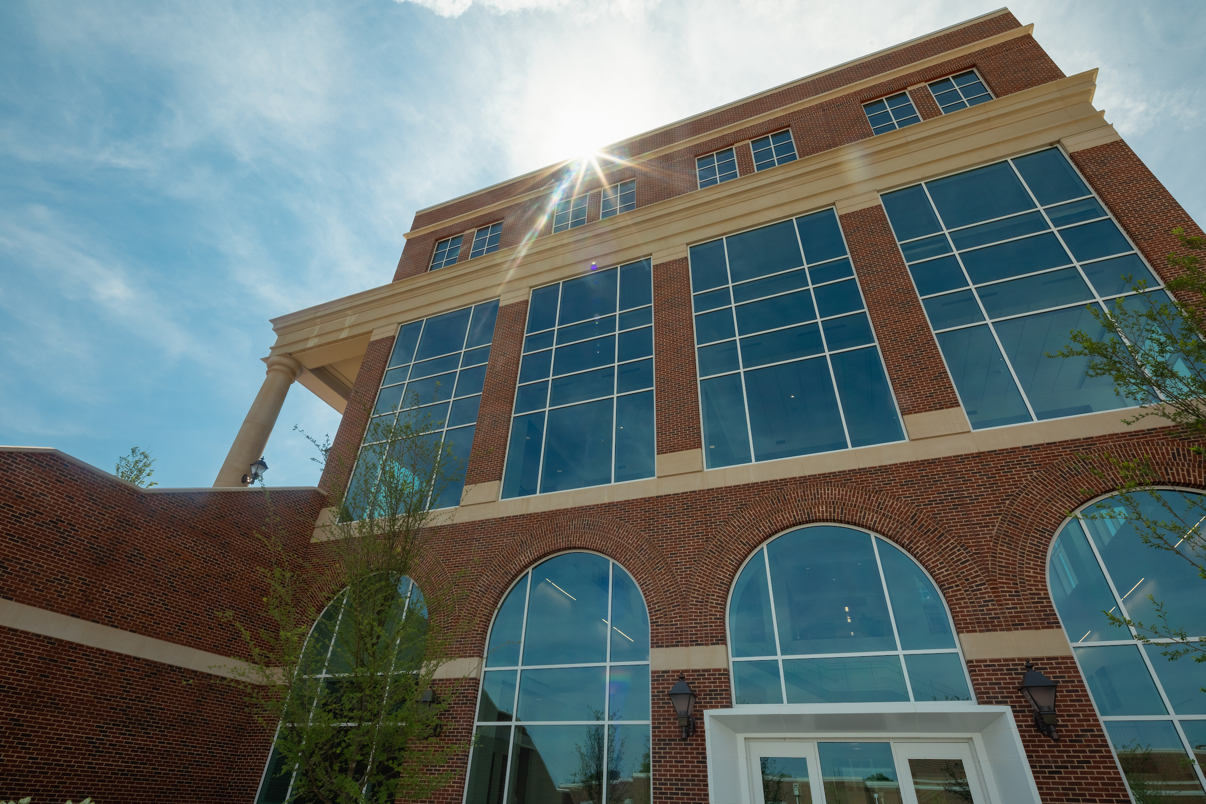 Sun shining brightly past beautiful brick building with large windows on Central Piedmont’s Harper Campus.