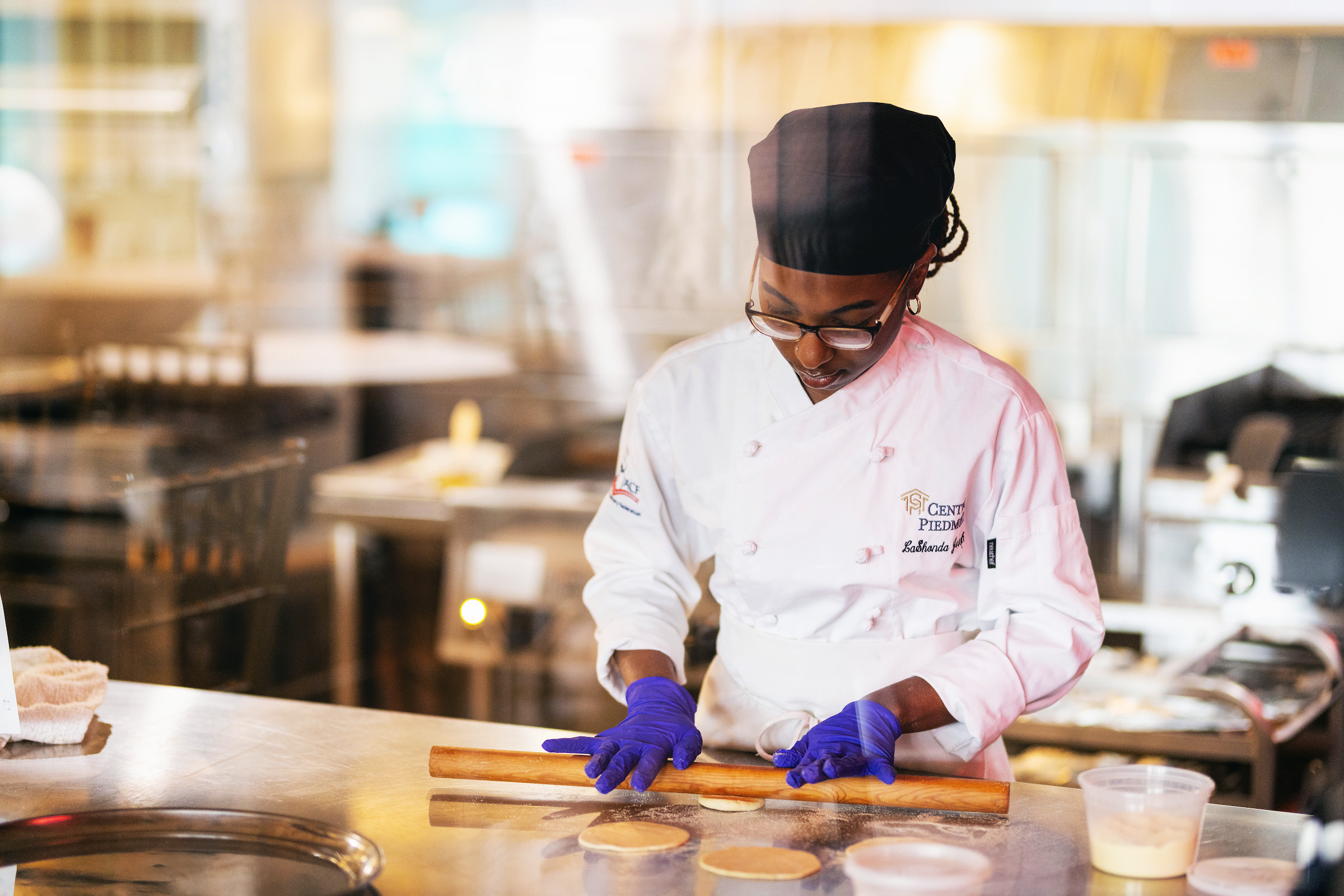 Culinary student in a chef's coat and toque preparing food in a teaching kitchen