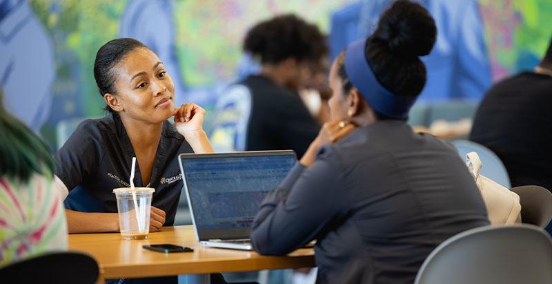Adviser talking with a student across a table with a laptop