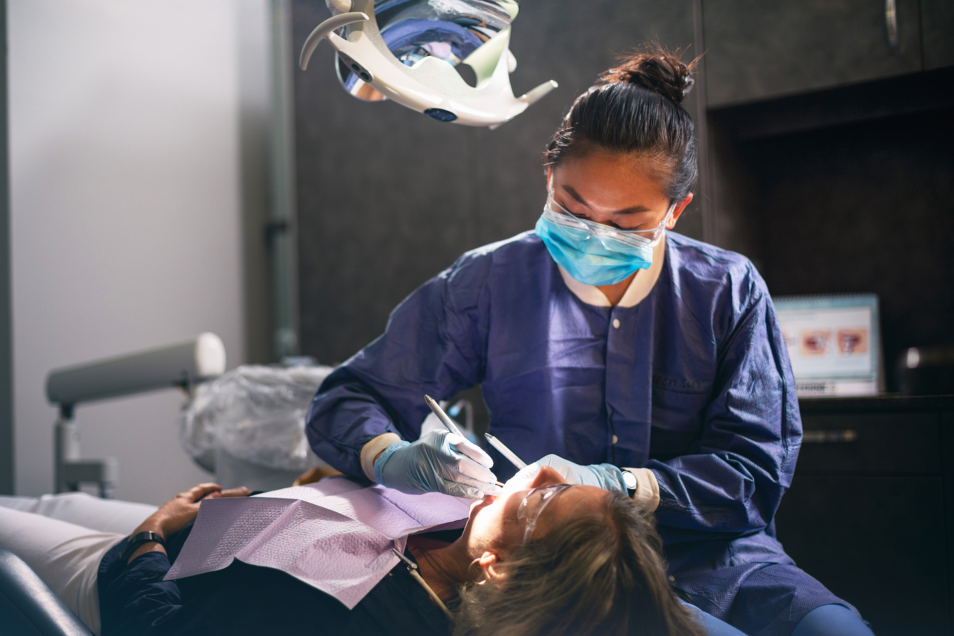 Central Piedmont student wearing a mask and cleaning a patient’s teeth inside dentist’s office.